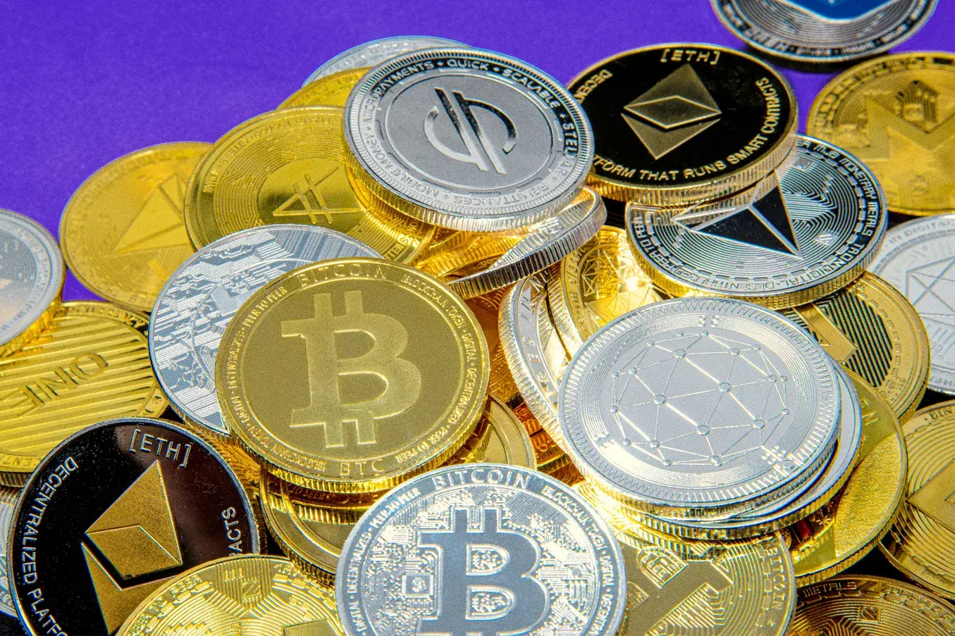 A pile of physical cryptocurrency tokens including Bitcoin and Ethereum coins in gold and silver