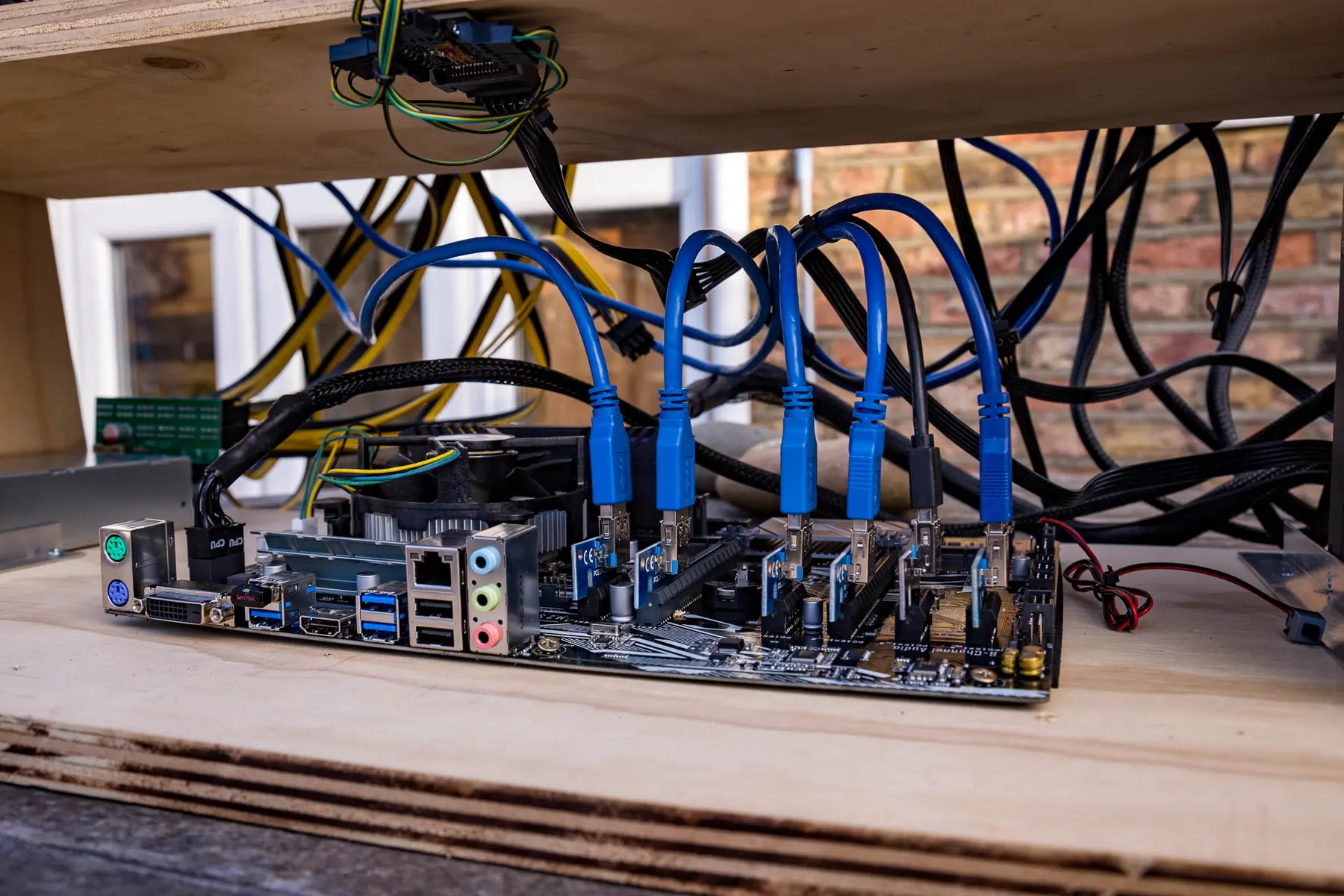 Close-up of a cryptocurrency mining rig with multiple GPUs connected via blue riser cables to a motherboard
