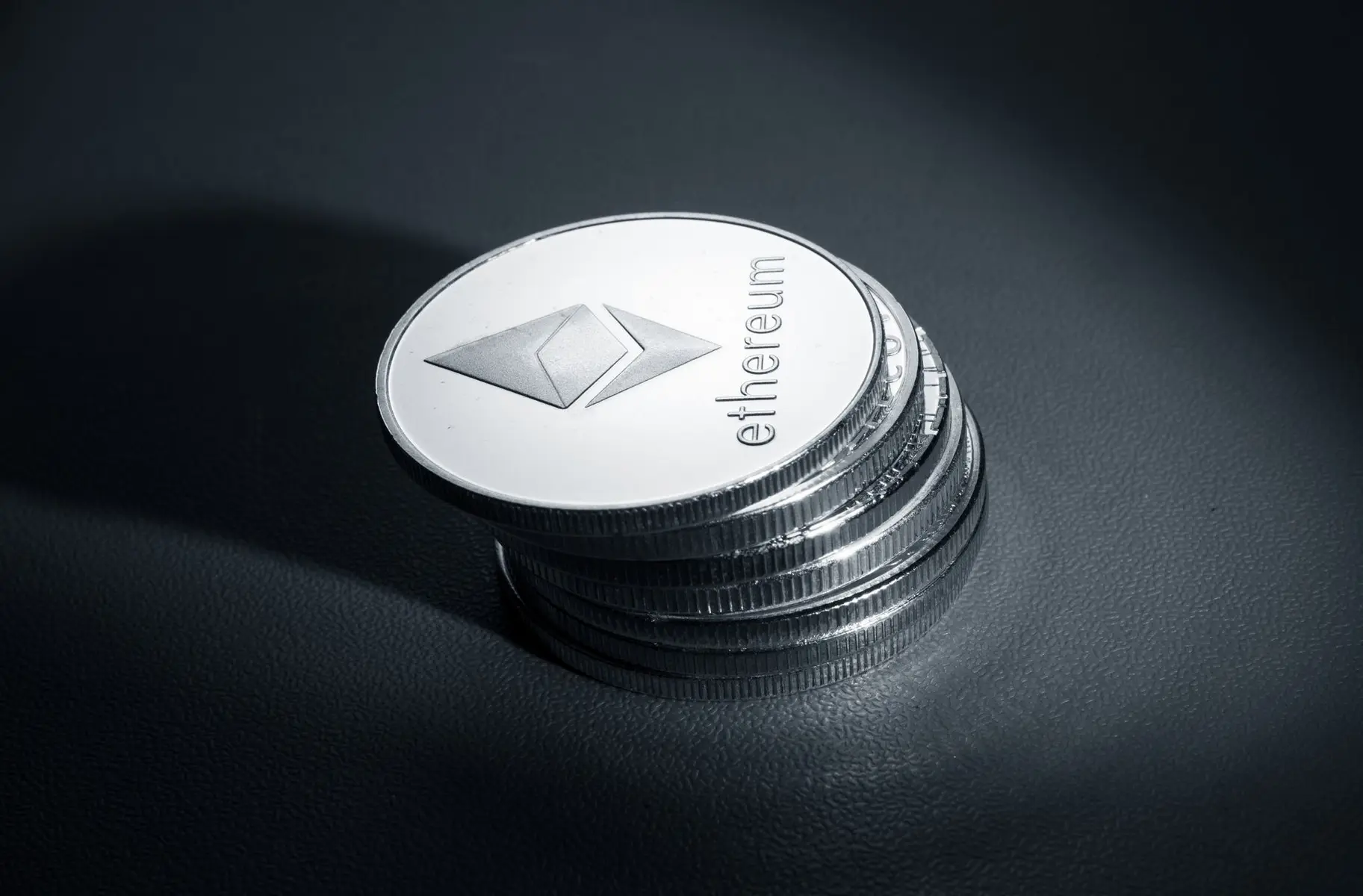 A stack of silver physical Ethereum cryptocurrency coins on a dark textured surface