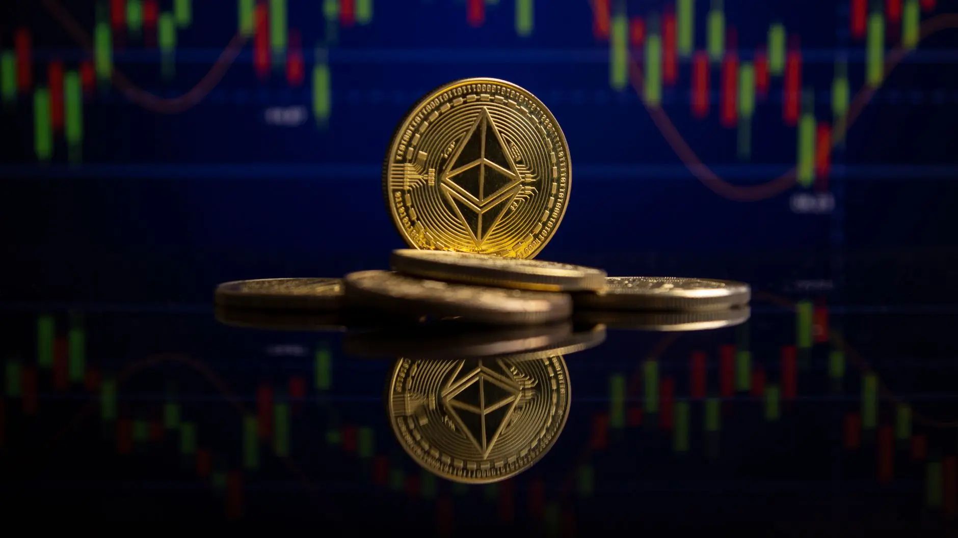 Gold Ethereum coins stacked in front of a blurred digital cryptocurrency trading candlestick chart