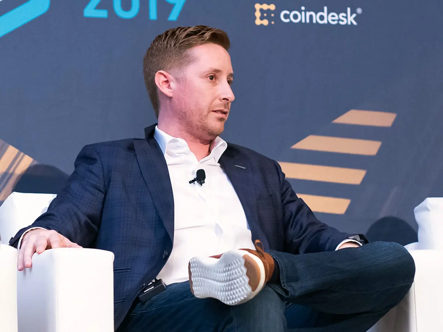 Zac Prince wearing a navy blazer and white shirt, seated at a Coindesk event