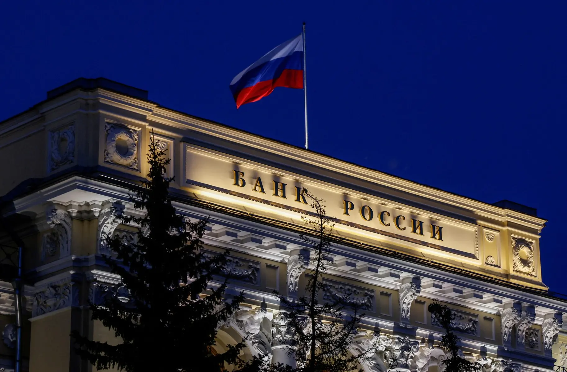 Illuminated facade of the Bank of Russia building in Moscow at night with the Russian flag flying above