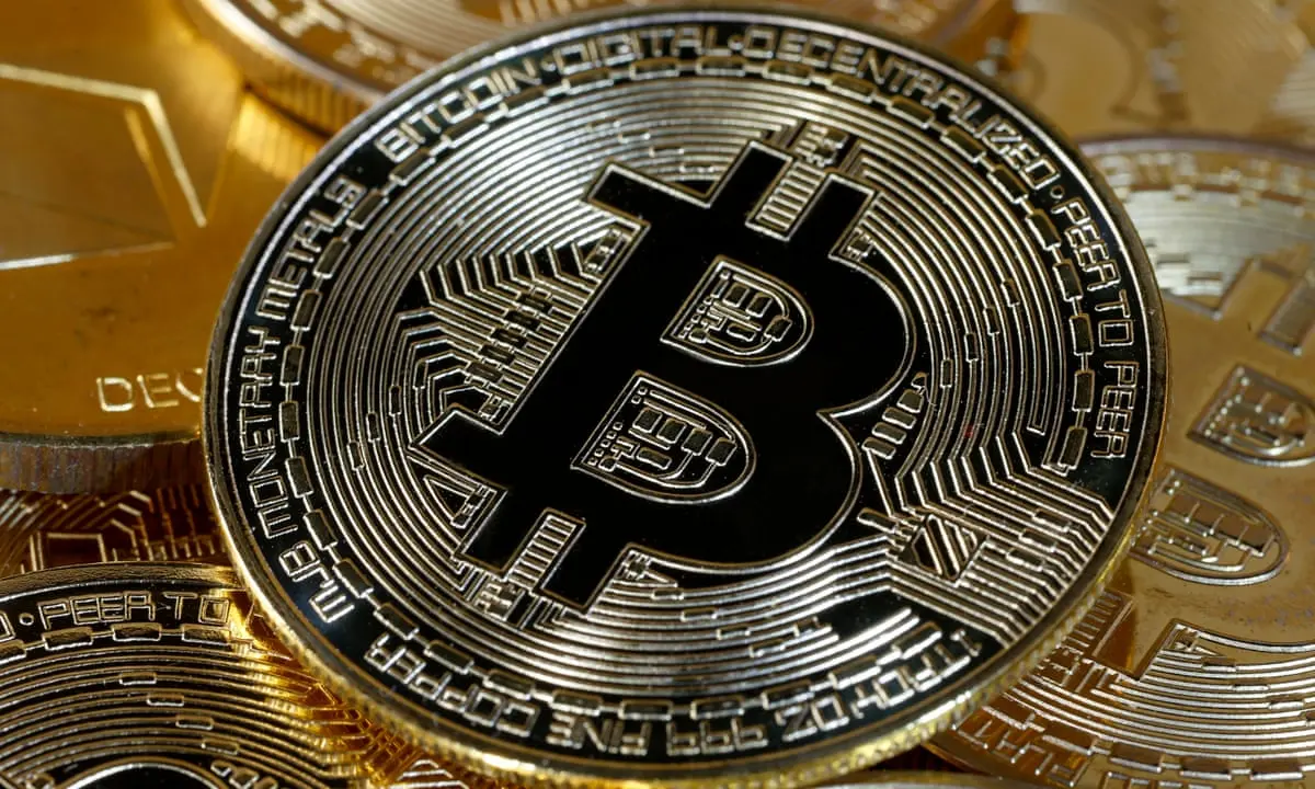 Close-up of a gold-colored physical Bitcoin coin with the B symbol centered on a circuit-board pattern.
