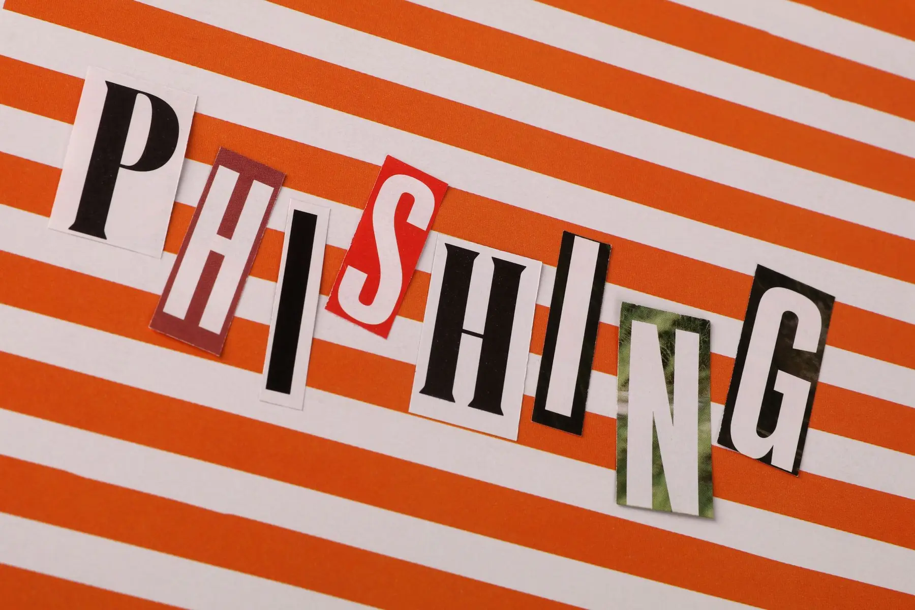 The word PHISHING spelled out in mismatched cutout magazine letters on an orange and white striped background