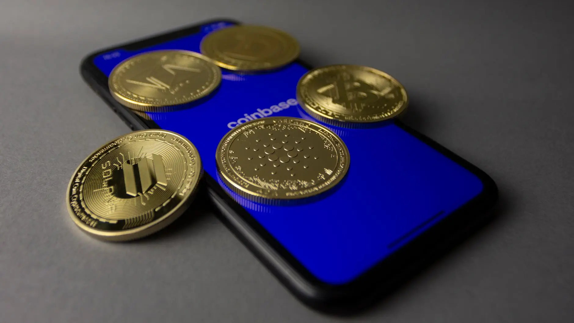 Physical gold-colored cryptocurrency coins resting on a smartphone displaying the Coinbase app