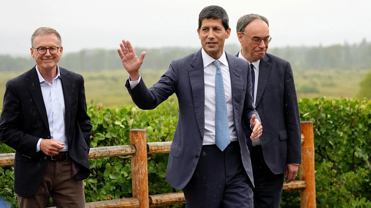 Kevin Warsh wearing a dark blue suit and light blue tie, gesturing while walking outdoors with two men.