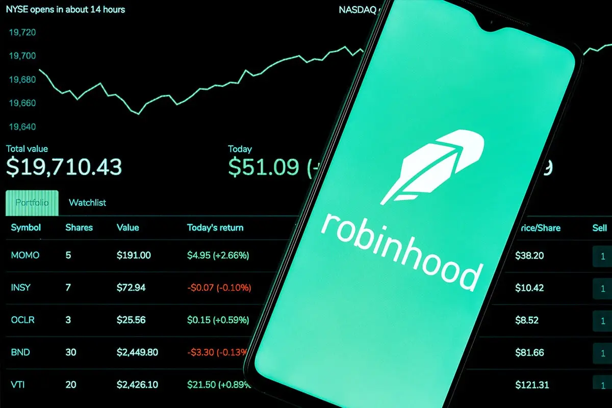 Robinhood app logo on a smartphone screen in front of a stock portfolio dashboard