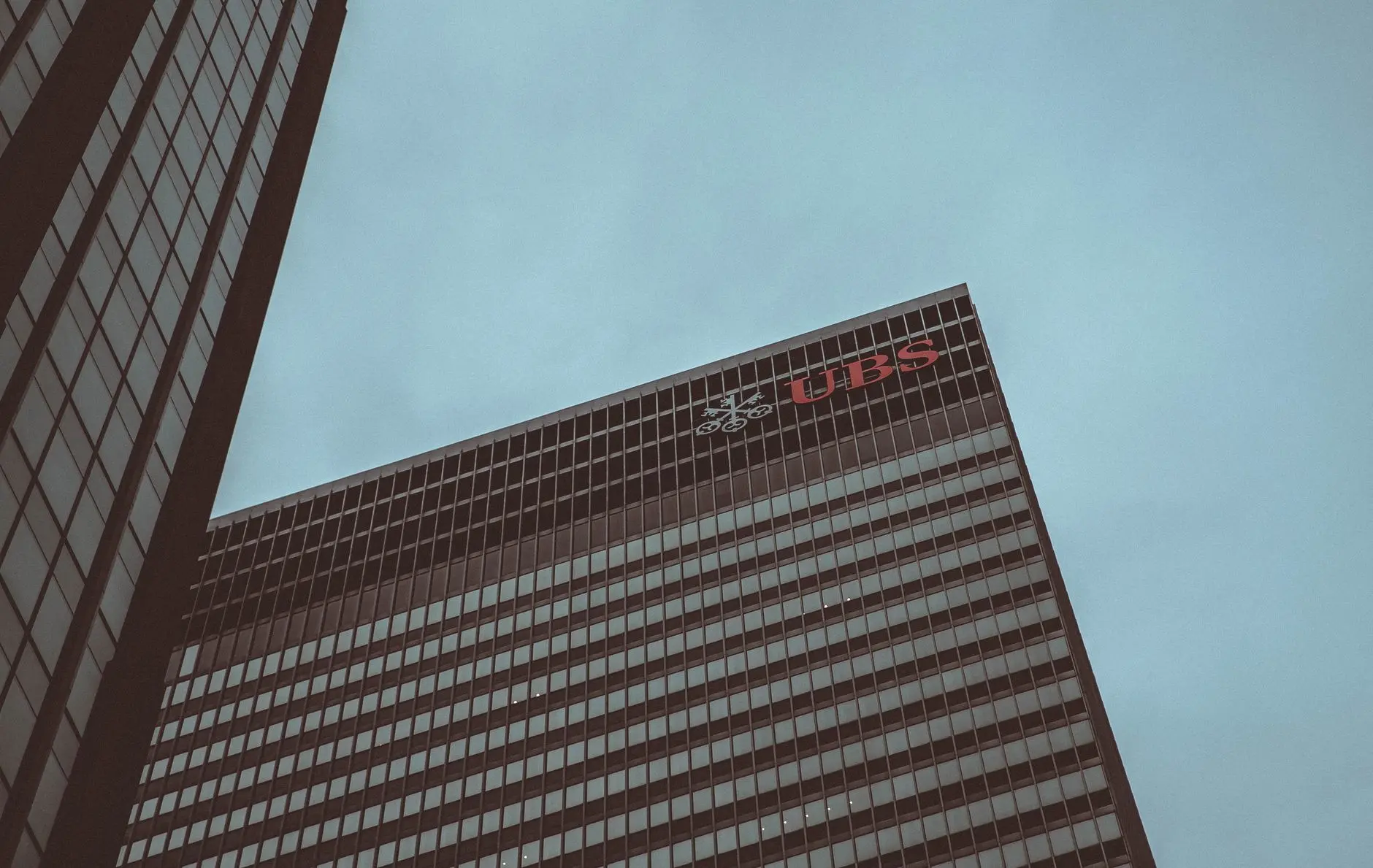 Low-angle shot of a UBS bank headquarters skyscraper with the red UBS logo at the top against a clear sky