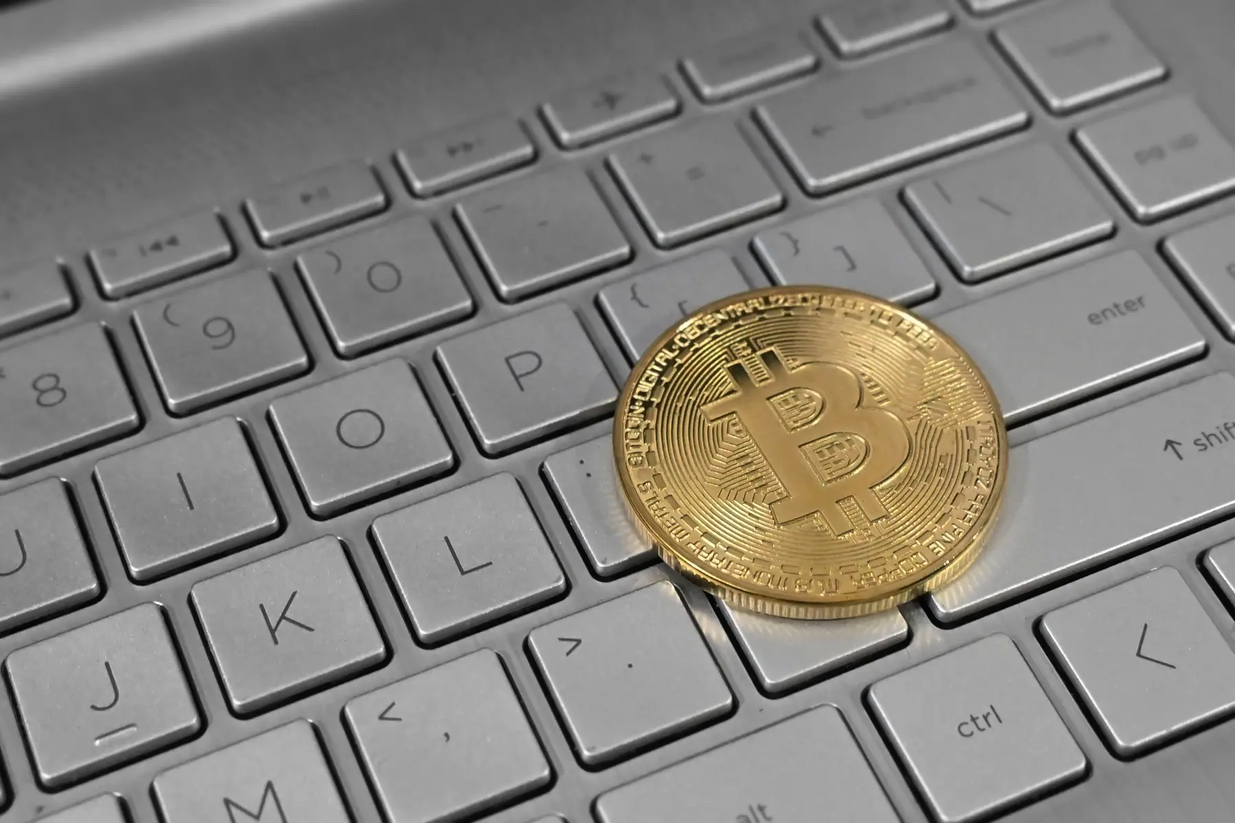 Uma moeda física de Bitcoin dourada apoiada sobre o teclado de um notebook prata.